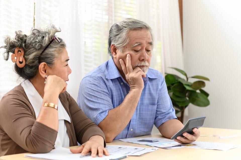 A visibly worried couple using a calculator to analyze bills and financial statements sitting on a table.