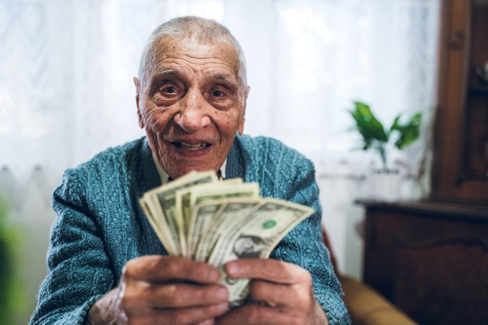 A smiling person is holding an assorted pile of fanned cash bills.