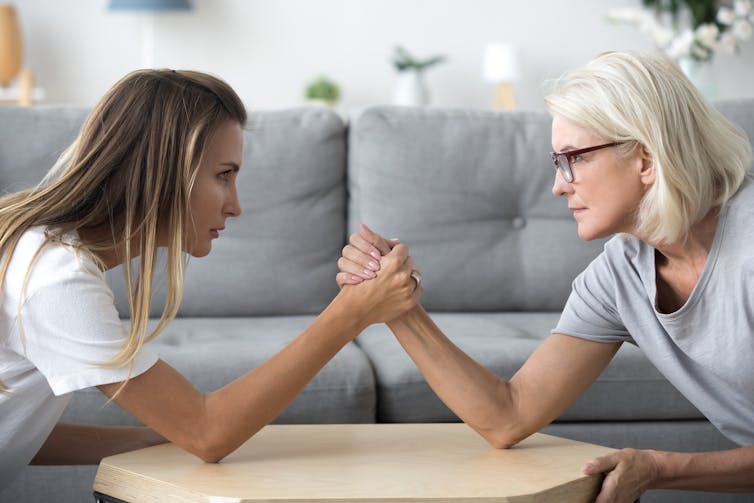 Two women from different generations arm wrestling.